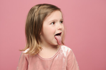 Funny little girl showing her tongue on pink background
