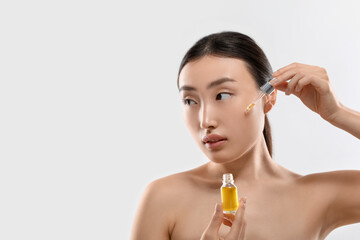 Fototapeta premium Beautiful young woman applying cosmetic serum onto her face on white background, space for text