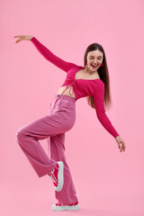 Beautiful young woman in pink clothes dancing on color background