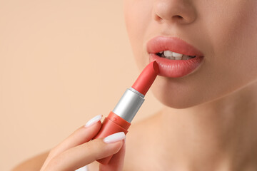 Young woman applying lipstick on light background, closeup