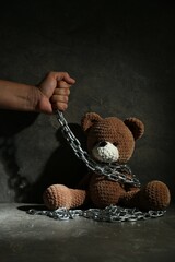 Stop child abuse. Man holding chain with toy bear in dark room, closeup