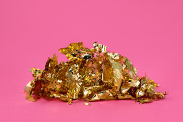 Pieces of edible gold leaf on pink background, closeup