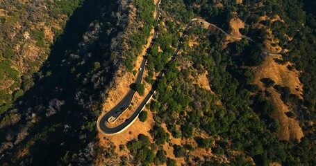 Black and white car running to face each other at the dangerous loop of mountain road. Bird's eye view on the rock with road on in sunny California.