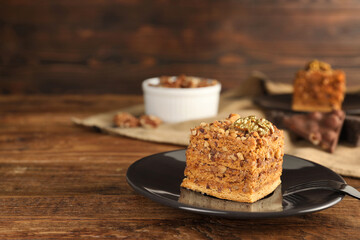 Piece of honey cake with walnuts and fork on wooden table, closeup with space for text