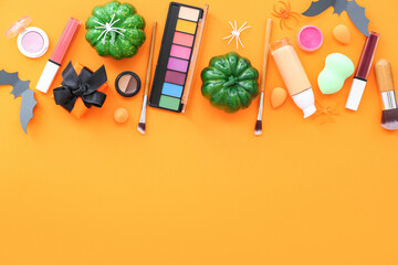 Fototapeta na wymiar Makeup products and Halloween decor on orange background