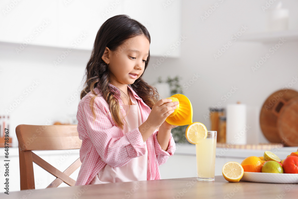 Canvas Prints Little Asian girl making fresh citrus juice at table in kitchen