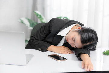 Sleepy and tired young Asian businesswoman or female offie worker taking nap or sleep on her office desk.