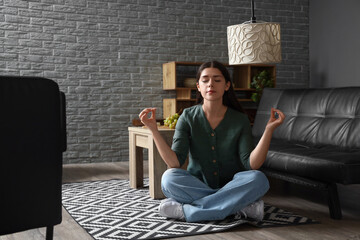 Young woman meditating on carpet in living room