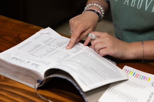 Close up of woman's hands holding highlighter and pointing to text on table of contents page in open Bible during Bible study group