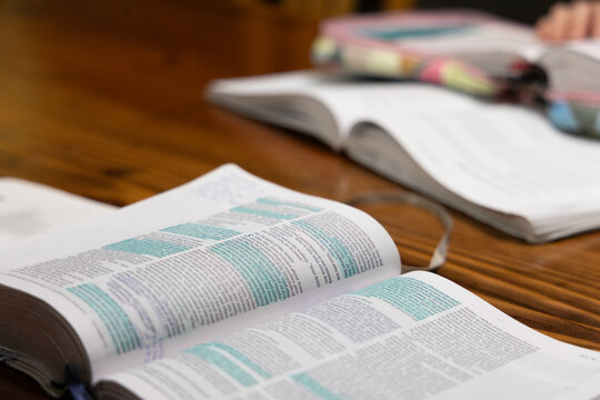 Open Bible laying on table with blue highlighter on pieces of text with another Bible and study book in background
