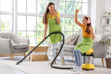 Little girl in headphones and her mother with vacuum cleaner at home