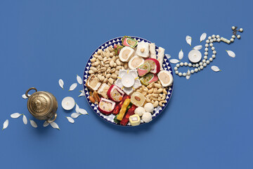 Diya lamp with candles, beads and plate of different treats on blue background. Divaly celebration