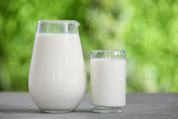 Glass and jug of fresh milk on grey table outdoors