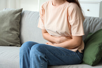 Young woman sitting on sofa and suffering from abdominal pain at home