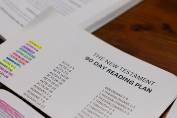 Fototapeta premium Close up of New Testament 90-Day Reading Plan sheet on wooden table next to study booklet for Bible study