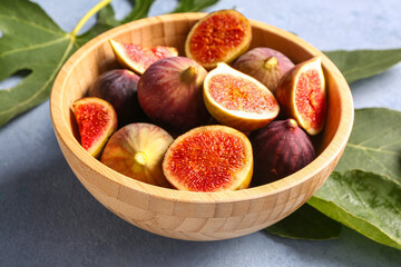 Bowl with ripe fresh figs and plant leaves on grunge blue background