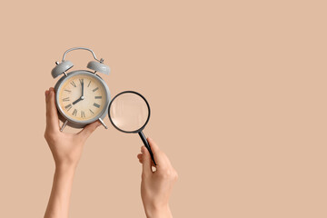 Female hands holding alarm clock and magnifier on beige background