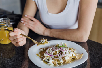 latin woman eating mexican chilaquiles for breakfast in morning in kitchen at home in Mexico, hispanic female in Latin America