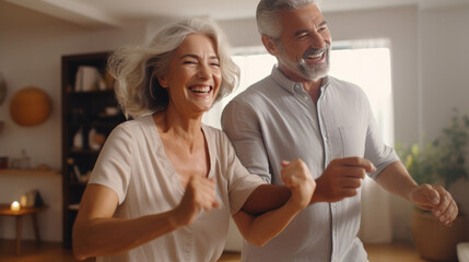 Fototapeta premium Keep moving. Romantic senior family couple wife and husband dancing to music together in living room, smiling laughing retired man and woman having fun, enjoying free time together at home