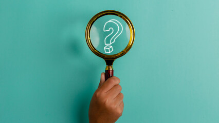 Hand holding a magnifying glass with a question mark icon on the blue background with copy space....