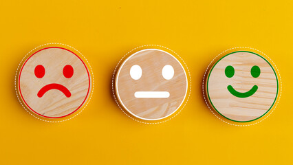 Concept of customer satisfaction. Happy sad and neutral smile faces on wooden blocks on a yellow background. Customer satisfaction, evaluation, or feedback concept.