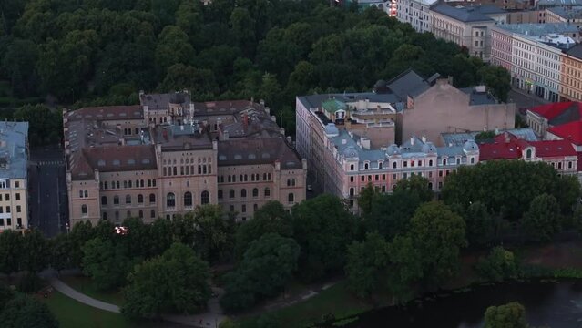 Aerial view of large palaces surrounded by grown trees in park. Tilt up reveal cityscape at dusk. Riga, Latvia