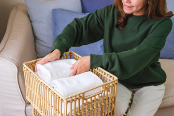 Closeup image of a woman folding and putting towel into a wooden basket at home