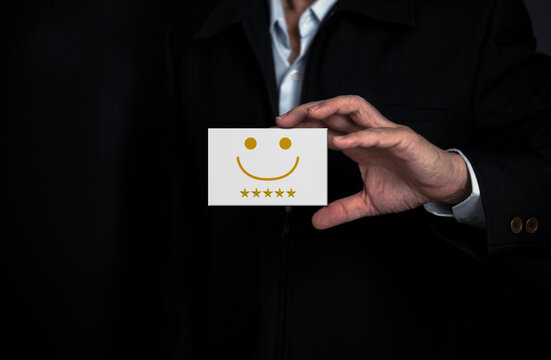 Satisfaction survey concept,Businessman hand holding card to show the smiling face emoticon  and give five star symbol to increase rating of products and services .
