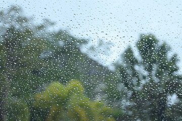blur background with blue sky and green tree on rainy day, water droplet on mirror