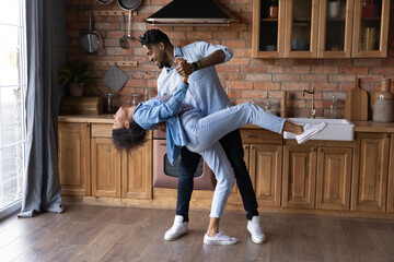 Excited African American loving young couple dancing in kitchen, enjoying romantic date, happy wife...