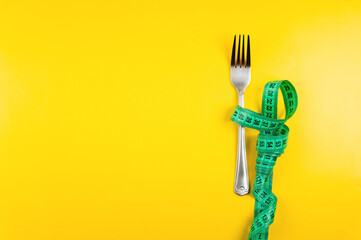 bright green measuring tape with a fork lies on a yellow background, top view. Healthy food idea go...