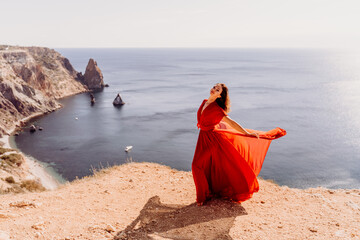 Woman red dress sea., posing on a rocky outcrop high above the sea. Girl on the nature on blue sky background. Fashion photo.