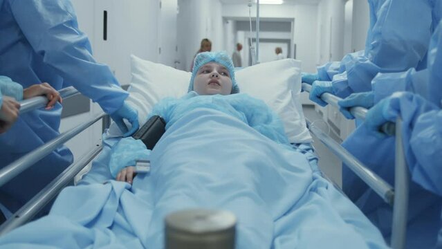 Doctors, paramedics and mom of kid push stretcher with sick young girl to surgery room. Woman supports lying on gurney daughter. Medical staff work in emergency department. Tracking shot. Slow motion.