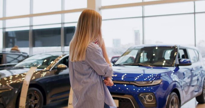 Young Cunning Woman Thinking About How To Convince Her Husband To Buy New Car Slow Motion Back Rare View. Puzzled Girl Cannot Choose A Vehicle In Auto Dealership Store.