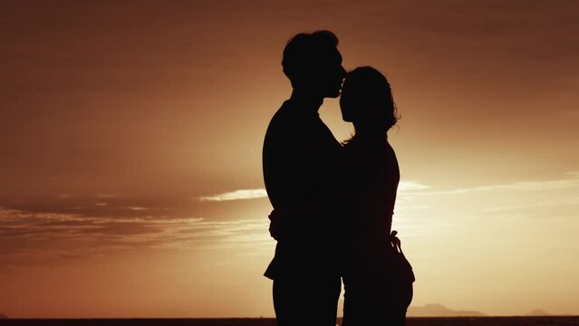 Male and female stand in an embrace in the morning near the sea. Silhouette of a loving family at sunrise or sunset. Husband hugs his wife, in the morning at sunrise. Family love concept.