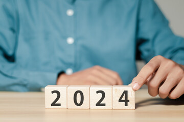 Starting business in the new year 2024 concept. Businessman arranges wooden blocks with text 2024. Financial planning and coping with change. - obrazy, fototapety, plakaty