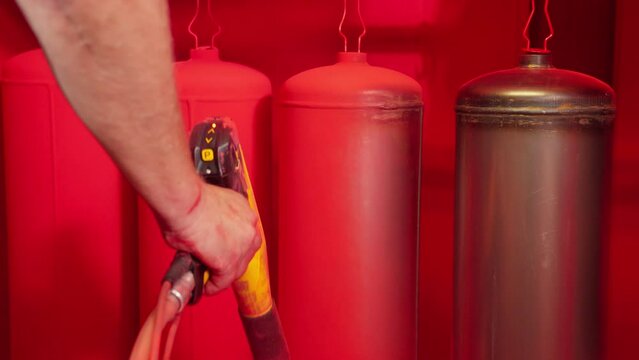 Worker paints fire extinguishers with spray gun at factory. Painting factory parts with special sprayer paint. Powder coating. Painter working at industrial manufacture. Close-up in 4K, UHD
