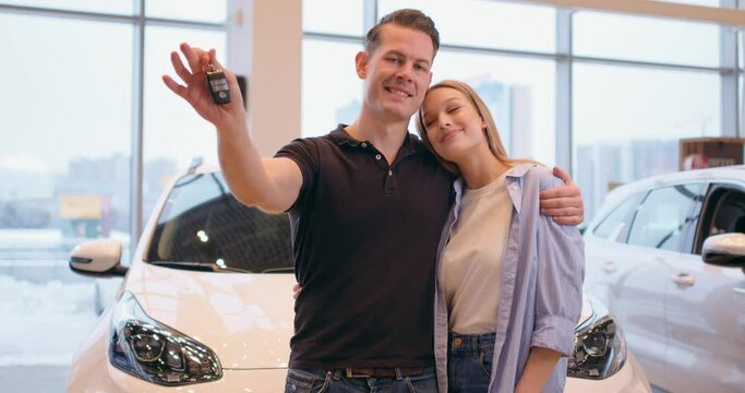 The concept of buying or renting a car. Young happy Caucasian couple with new car keys looking at camera, enjoying successful deal, bargain , purchase Slow motion Happiness dreams come true