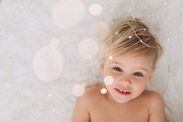 Naked child 2 years old lies and smiles at the lights from the garland