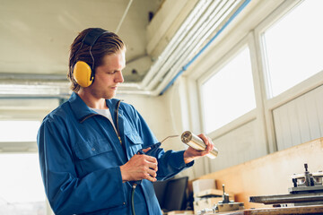 Focused young man in earmuffs standing with tools in factory