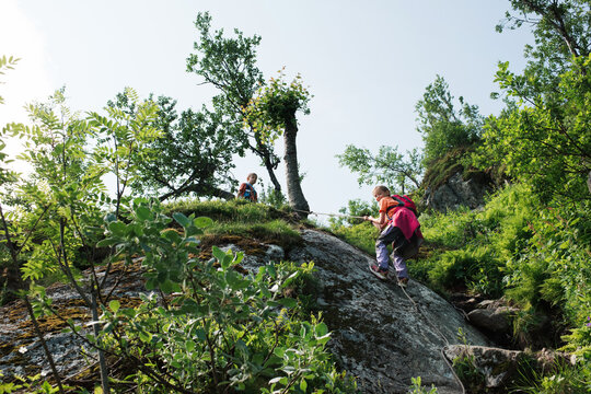 girl climbing up the side of a rock on a mountain with a rope
