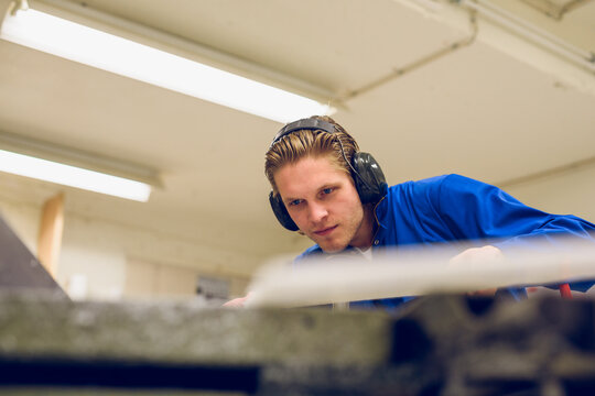 Focused young craftsman working in earmuffs at workbench in daylight