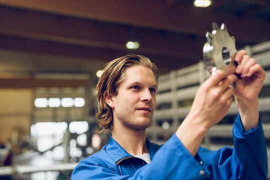 Young technician checking machine part in workshop