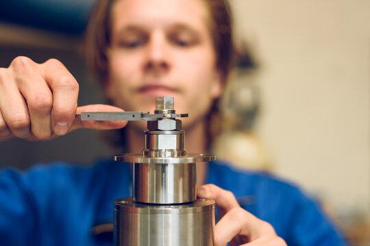 Focused young crop man tightening screw of machine in blurred factory