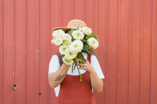 A woman near a red shed holding a boquet of White giant zinnia f