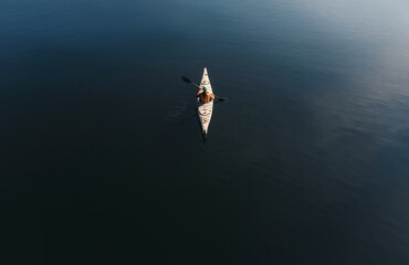 Overhead aerial view of woman paddling kayak on dark blue water.