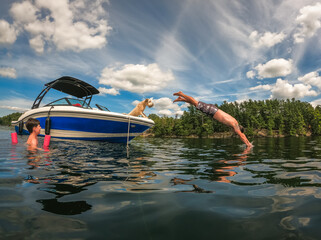 Man diving off boat into lake on summer day as dog and child watches.