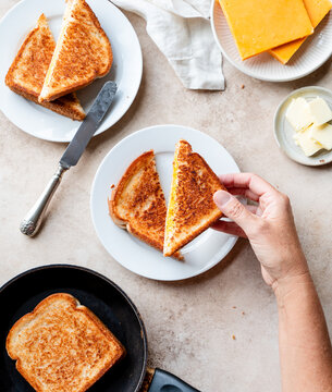 Top view of hand picking up grilled cheese sandwich off plate.