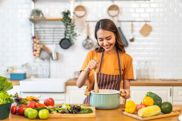 Young woman standing near stove and cooking, housewife, meal, chef, food.Happy woman looking and smelling tasting fresh delicious from soup in a pot with steam at white interior kitchen