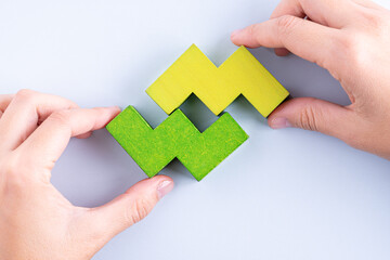 Hand holding wooden puzzle element. Hand sets the last element of the puzzle. The concept of logical thinking. Geometric shapes on a wooden background. Wooden blocks.